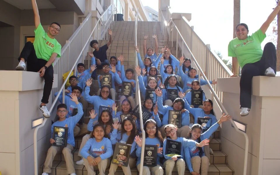 Immokalee Community Academy National Beta Club students and staff celebrating on outdoor stairs while holding awards and plaques.